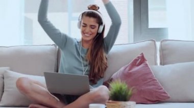 Motive olmuş genç bir kadının evdeki kanepede oturmuş laptopuyla dans edip müzik dinlediği bir video..