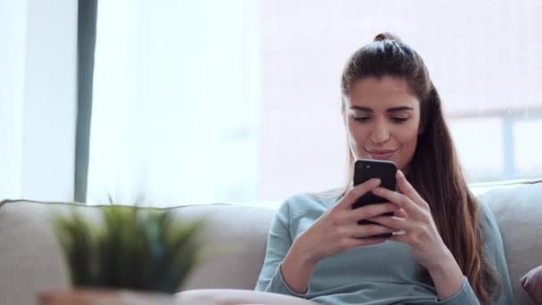 自宅でソファに座っている間に携帯電話で音楽を聴いているかなり若い女性のビデオ — ストック動画