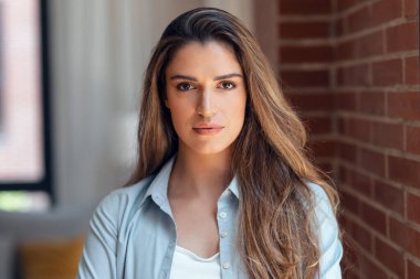 Evdeki oturma odasında kameraya bakan konsantre genç bir kadının portresi..