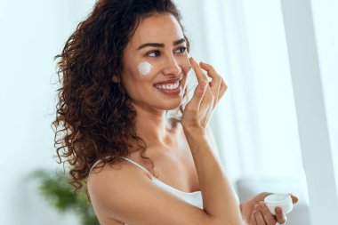 Evdeki aynaya bakarken cildine özen gösteren güzel genç bir kadının portresi..