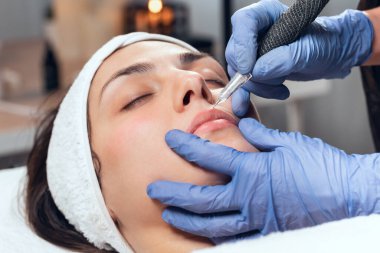 Kozmetik uzmanının, spa merkezinde sedyede yatarken, gençleştirme için yüzüne mikropigmentasyon iğnesi yaparken görüntüsü..