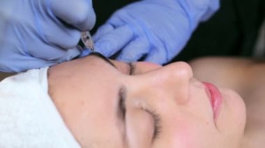 Kozmetik uzmanının spa merkezinde sedyede yatarken gözünün üzerine mikro pigmentasyon iğnesi yaptığı video..