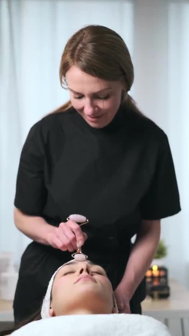 美容師のビデオは スパセンターでストレッチャーに横たわっている間 女性に若返りのための顔療法を作ります — ストック動画