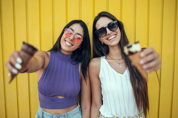 Strzelać Dwóch Pięknych Młodych Kobiet Jedzących Lody Podczas Zabawy Żółtym — Zdjęcie stockowe