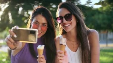 Parkta cep telefonuyla fotoğraf çekilirken dondurma yiyen iki güzel genç kadının videosu..
