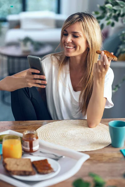 Портрет Улыбающейся Молодой Женщины Наслаждающейся Завтраком Используя Свой Мобильный Телефон — стоковое фото