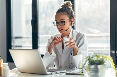 Konsültasyondaki dizüstü bilgisayar ve kulaklıkla hastaya tıbbi tedaviyi açıklarken kadın doktorun konuşması..