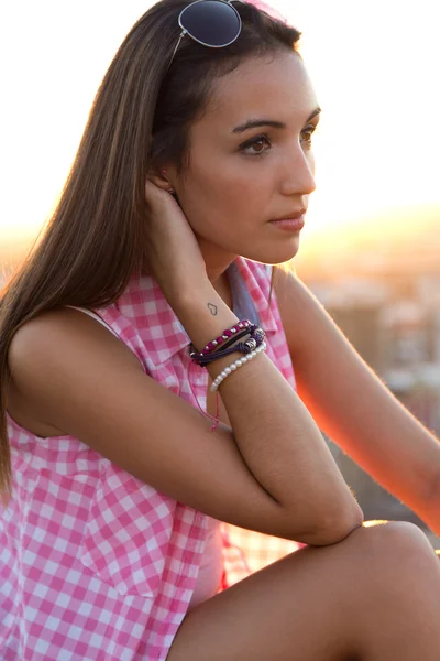 Mooi meisje zit op het dak bij zonsondergang. — Stockfoto