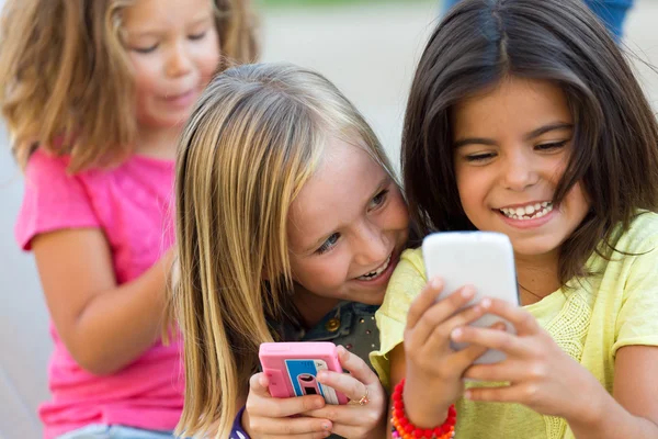 Grupo de niños charlando con teléfonos inteligentes en el parque . — Foto de Stock