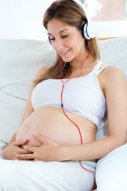 Hamile kadın kanepede oturup kulaklıkla müzik dinliyor..