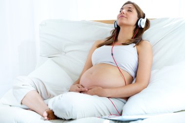 Hamile kadın kanepede oturup kulaklıkla müzik dinliyor..