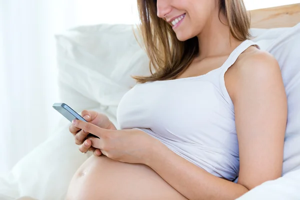 Zwangere vrouw met behulp van haar mobiele telefoon op sofa. — Stockfoto