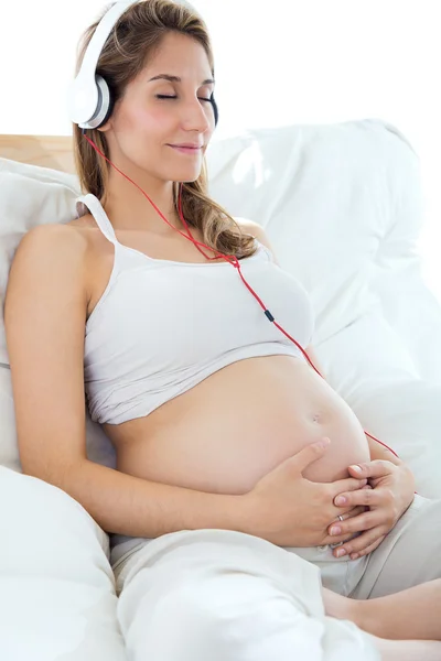 Zwangere vrouw zit op de bank en het luisteren naar muziek in koptelefoon. — Stockfoto