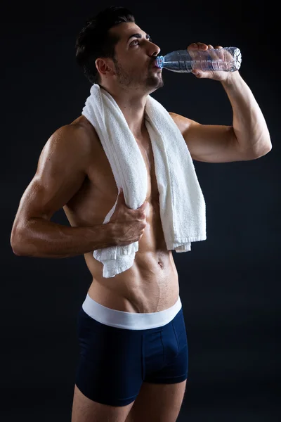 Beautiful and muscular man drinking water in dark background. — Stock Photo, Image