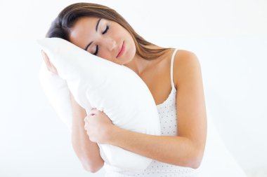 Beautiful young woman holding a pillow and slepping on bed.