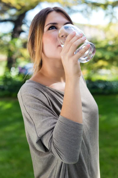 Porträt eines schönen Mädchens, das Wasserglas im grünen Park trinkt. — Stockfoto