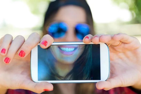 Открытый портрет красивой девушки, делающей селфи с мобильным телефоном в городе . — стоковое фото