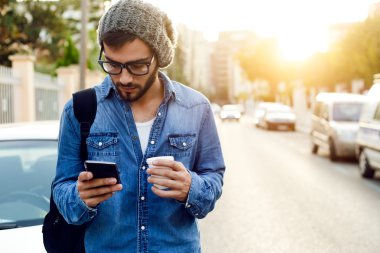 Modern young man with mobile phone in the street. clipart