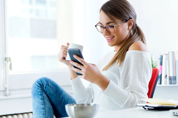 Ganska ung kvinna med hennes mobiltelefon på kontoret. — Stockfoto