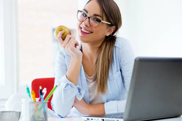 Bardzo młoda kobieta jedzenie jabłka w jej biurze. — Zdjęcie stockowe