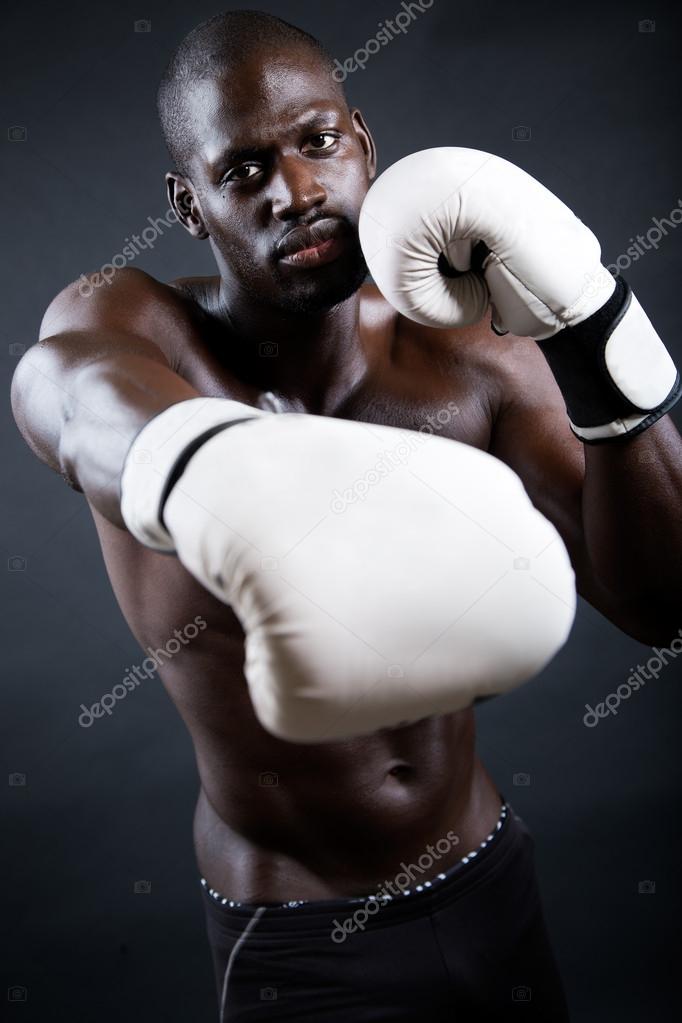 Young athletic boxer wearing gloves in black background. 