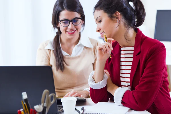 Dos jóvenes empresarias que trabajan con laptop en su oficina . — Foto de Stock