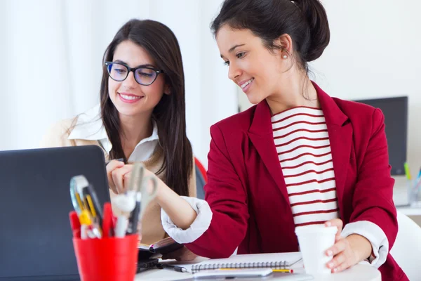 Dos jóvenes empresarias que trabajan con laptop en su oficina . — Foto de Stock