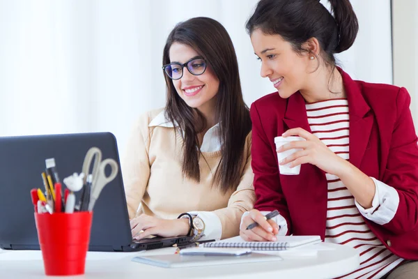 Deux jeunes femmes d'affaires travaillant avec un ordinateur portable dans son bureau . — Photo