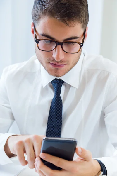 Jonge knappe man aan het werk in zijn kantoor met mobiele telefoon. — Stockfoto