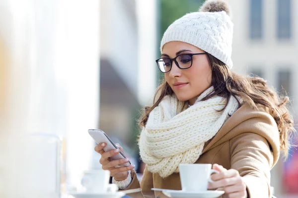 Giovane bella donna che utilizza il suo telefono cellulare in un caffè . — Foto Stock