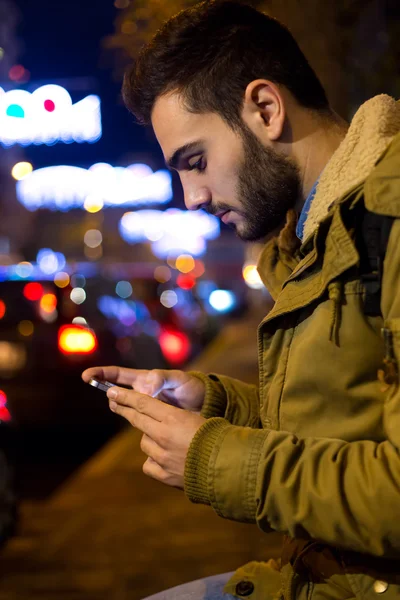 Portrait de jeune homme utilisant son téléphone portable dans la rue la nuit . — Photo