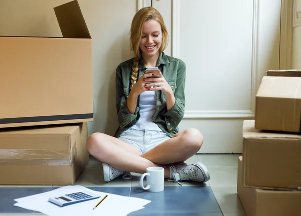 Jovem mulher bonita com telefone celular em sua nova casa . — Fotografia de Stock