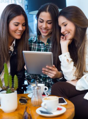 Dijital tablet kafe dükkanında kullanan üç genç kadın.