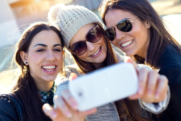 Drie studenten meisjes met behulp van mobiele telefoon in de campus. — Stockfoto