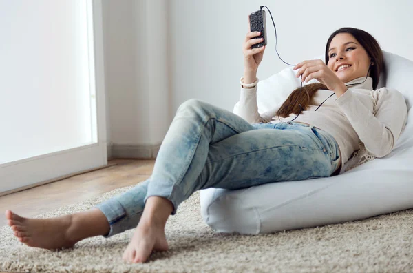 Молодая женщина слушает музыку мобильным телефоном у себя дома — стоковое фото