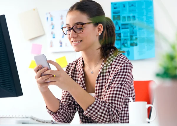 Belle jeune femme utilisant son téléphone portable dans le bureau . — Photo