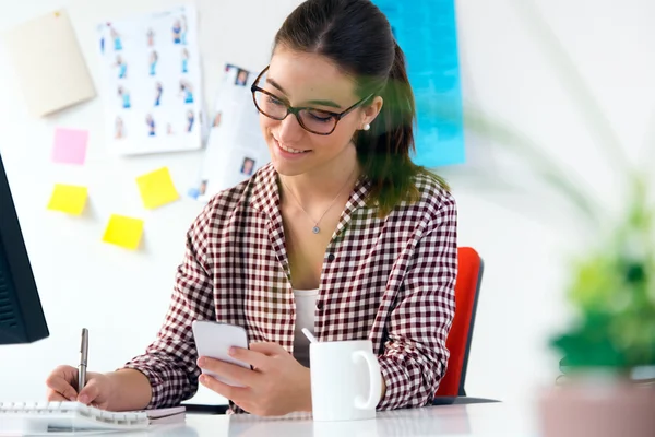 Belle jeune femme utilisant son téléphone portable dans le bureau . — Photo