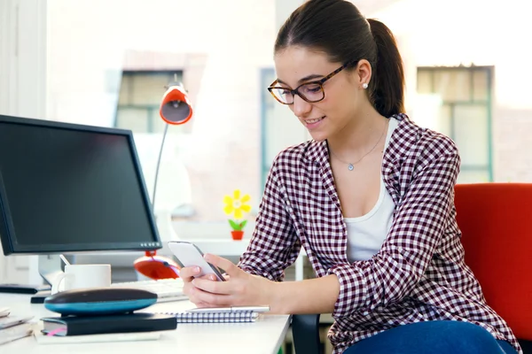 Schöne junge Frau mit ihrem Handy im Büro. — Stockfoto