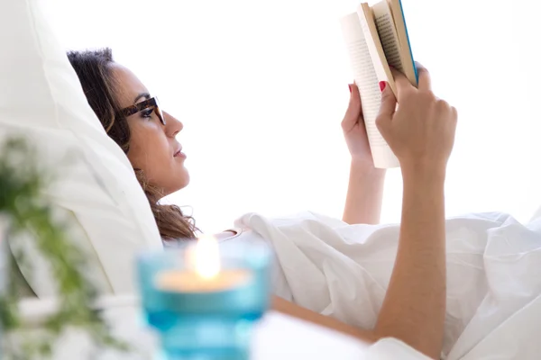Vacker ung kvinna läser en bok i sängen. — Stockfoto