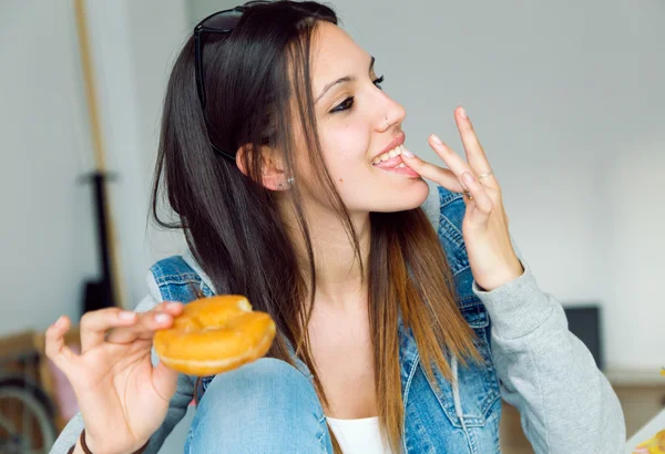 Όμορφη νεαρή γυναίκα τρώει ντόνατς στο σπίτι. — Φωτογραφία Αρχείου