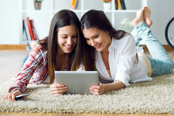 Dos hermosas amigas jóvenes usando tableta digital en casa . — Foto de Stock