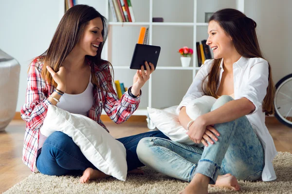 Duas belas jovens amigas usando tablet digital em casa . — Fotografia de Stock