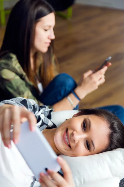 Två vackra unga kvinnan använder mobiltelefon hemma. — Stockfoto