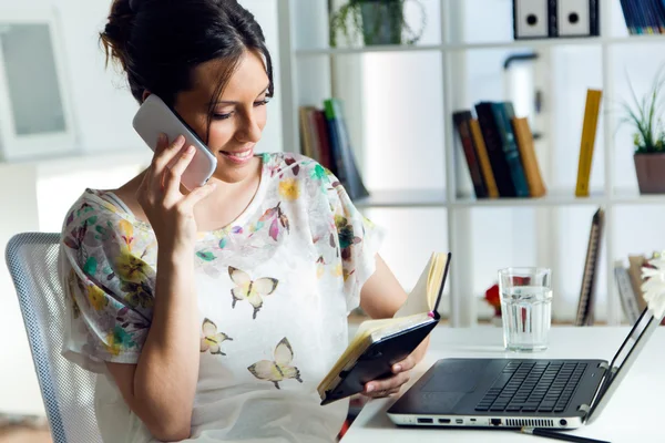 Jolie jeune femme utilisant son téléphone portable dans le bureau . — Photo