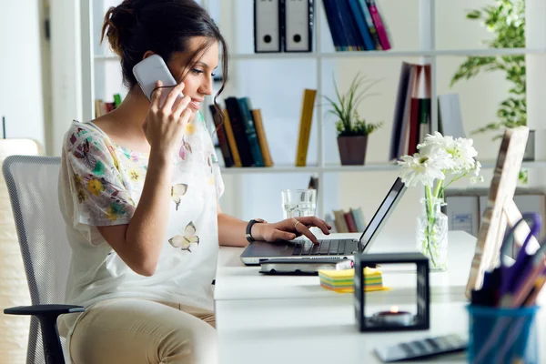 Jolie jeune femme utilisant son téléphone portable dans le bureau . — Photo