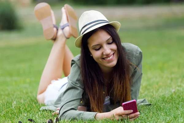 Mooie jonge vrouw met behulp van haar mobiele telefoon in het park. — Stockfoto