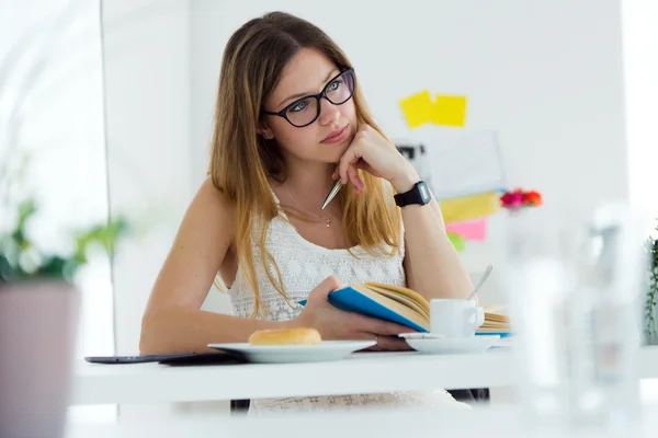 Mujer bastante joven leyendo un libro y desayunando en casa . — Foto de Stock