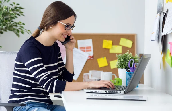 Vertrouwen jonge vrouw die in haar kantoor met een laptop werkt. — Stockfoto