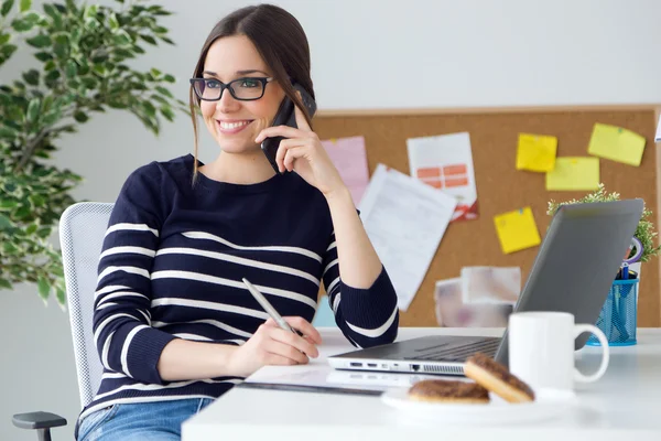 Vertrouwen jonge vrouw die werkt in haar kantoor met mobiele telefoon. — Stockfoto