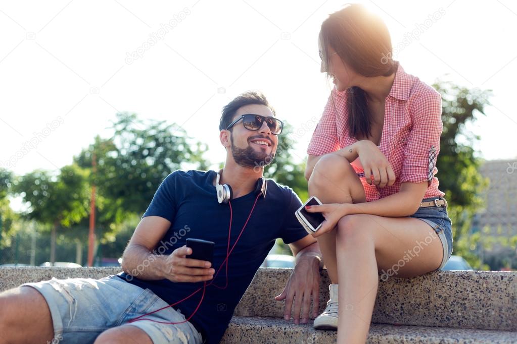 Two friends using mobile phone and listening to music in the str